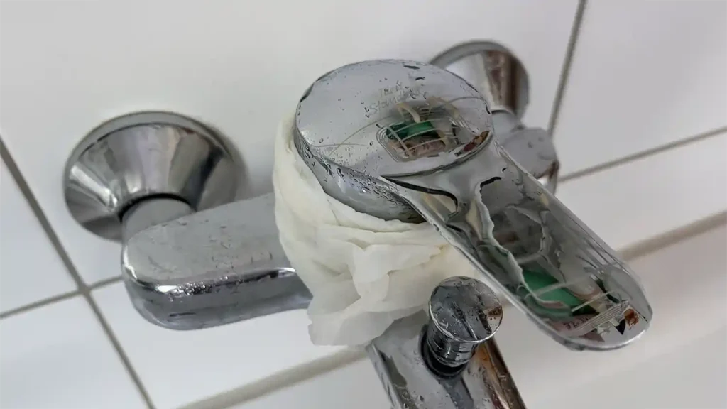 Verkalkter Wasserhahn wird mit FUSL Kalkreiniger gereinigt. Daf&uuml;r wird ein in Reiniger getr&auml;nktes Tuch um den Wasserhahn gewickelt um dem Reiniger mehr Zeit zum Wirken zu geben.