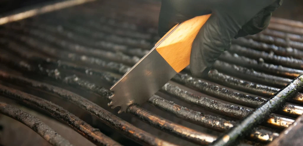 Ein dreckiger Grillrost wird mit einem Grillrost-Schaber gereinigt