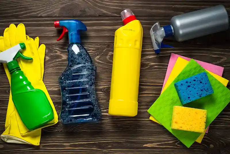 Verschiedene Reinigungsprodukte sowie Schw&auml;mme und T&uuml;cher liegen auf einem Holzboden
