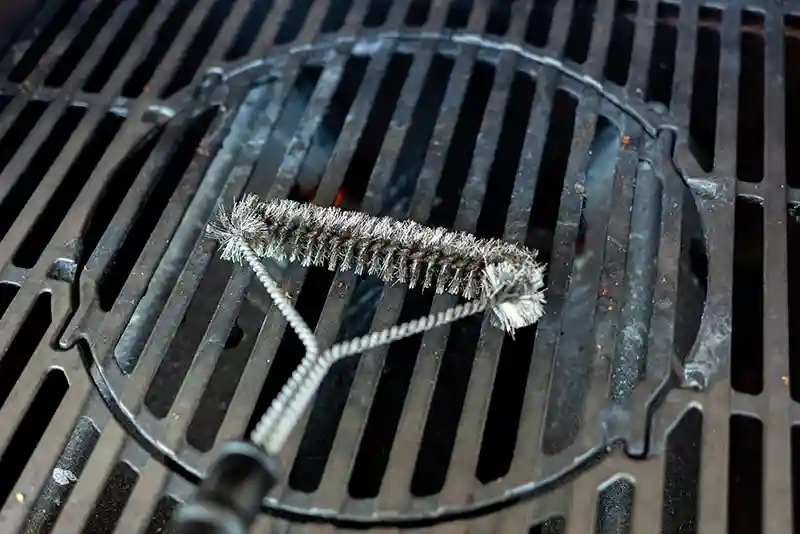 Reinigungsb&uuml;rste liegt auf einem dreckigen Grillrost