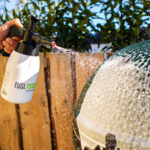 Aus einem Schaumdruckspr&uuml;her wird Reinigungsschaum auf einen gr&uuml;nen Keramikgrill gespr&uuml;ht